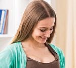 A woman in brown shirt and green jacket smiling.